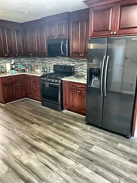 Kitchen with cherry cabinets, black stainless appliances and wood-look tile floor by Brown Sterling Builders
