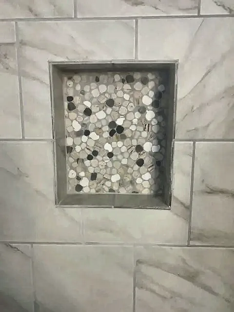 Tiled shower niche with pebble mosaic by Brown Sterling Builders